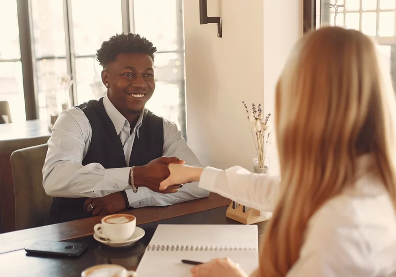 Two people shaking hands across a coffee-shop table after a first conversation (stock photo)