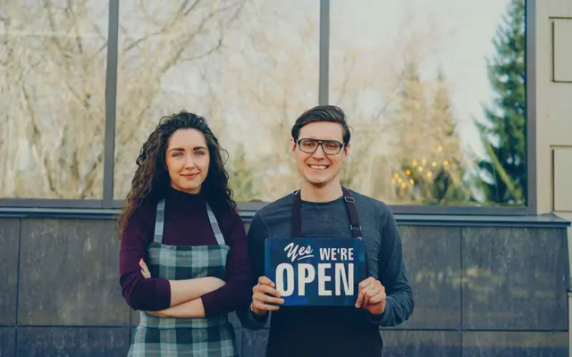 Two shop owners standing together holding an open sign (stock photo)